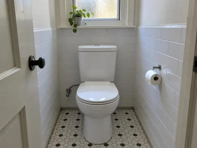 Clean white toilet in a tiled bathroom with window and patterned floor in Kingsford
