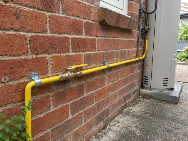 Yellow gas pipe and fittings along a brick exterior wall beside a unit in Kensington